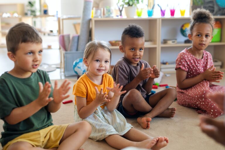 group-of-small-nursery-school-children-sitting-on-floor-indoors-in-classroom-clapping-768x512
